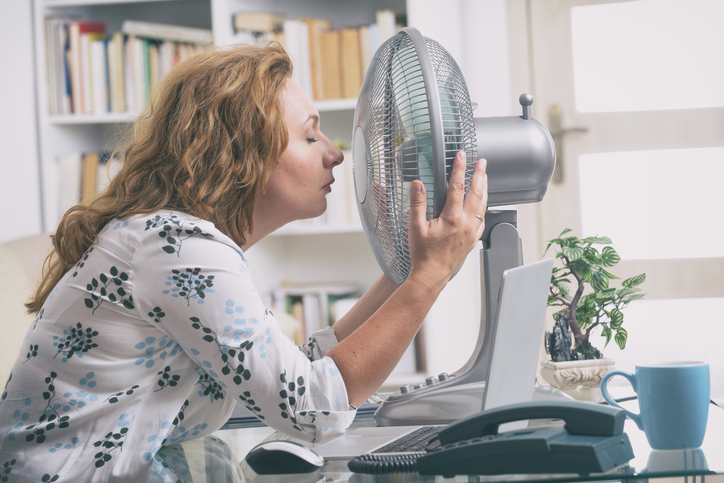 woman cooling off with a fan at her desk